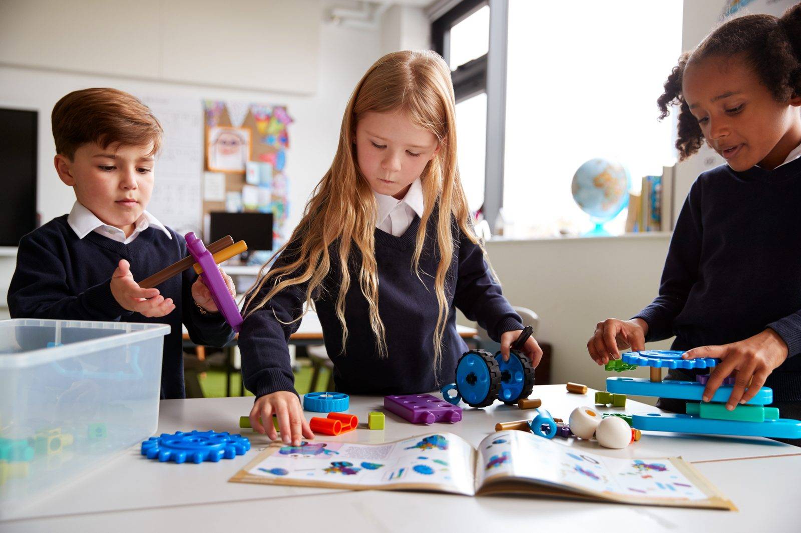 Three children building with plastic gears at a classroom table